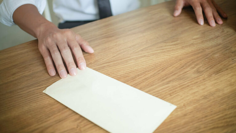 Man standing at brown desk touching a folded piece of paper.