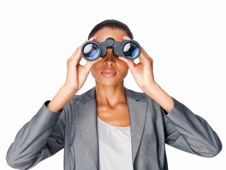 Woman in grey blazer looking through binoculars.