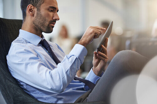 Businessman with shadow beard lounging in chair while looking intently at device.