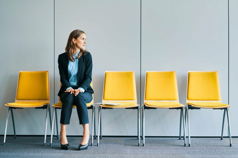 Businessman sitting alone in row of yellow chairs waiting for an interview.