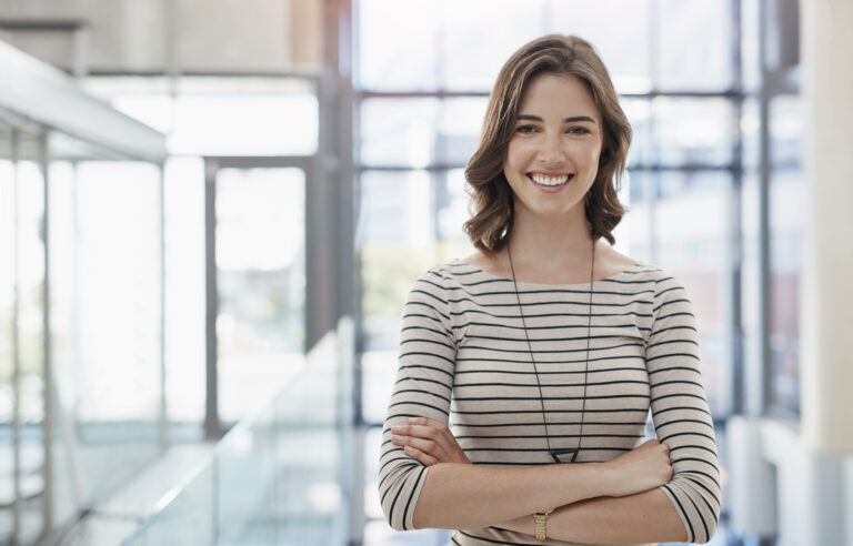 Young smiling businesswoman standing with arms crossed at the office.