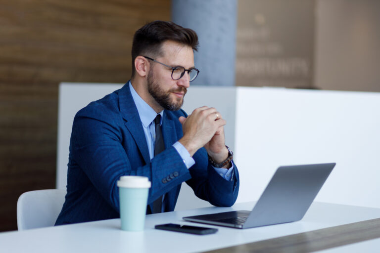 Professional businessman considering financial data on laptop in modern office, focused on work and technology