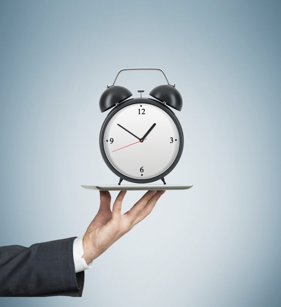 A man holds an alarm clock on a silver tray.