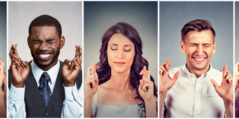 A series of side by side pictures. The pictures on the extreme left and right are cut off and all that is shown is a portion of hand crossing its fingers. Three images in the center are fully visible. The visible image on the left is of a professionally dressed African American man closing his eyes tightly, smiling, and crossing his fingers. The right most complete image is of a white man dressed in business casual attire who has a similar gesture as the man on the left. In the middle is a white woman who is also crossing her fingers but she has a more calm face as her eyes are only gently closed.