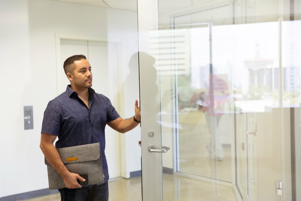 A young man seems to be entering the glass entry way of an office suite from the building's hallway.