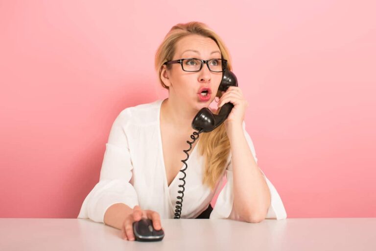 A woman talks excitedly on a older style telephone and moves a mouse with her other hand.