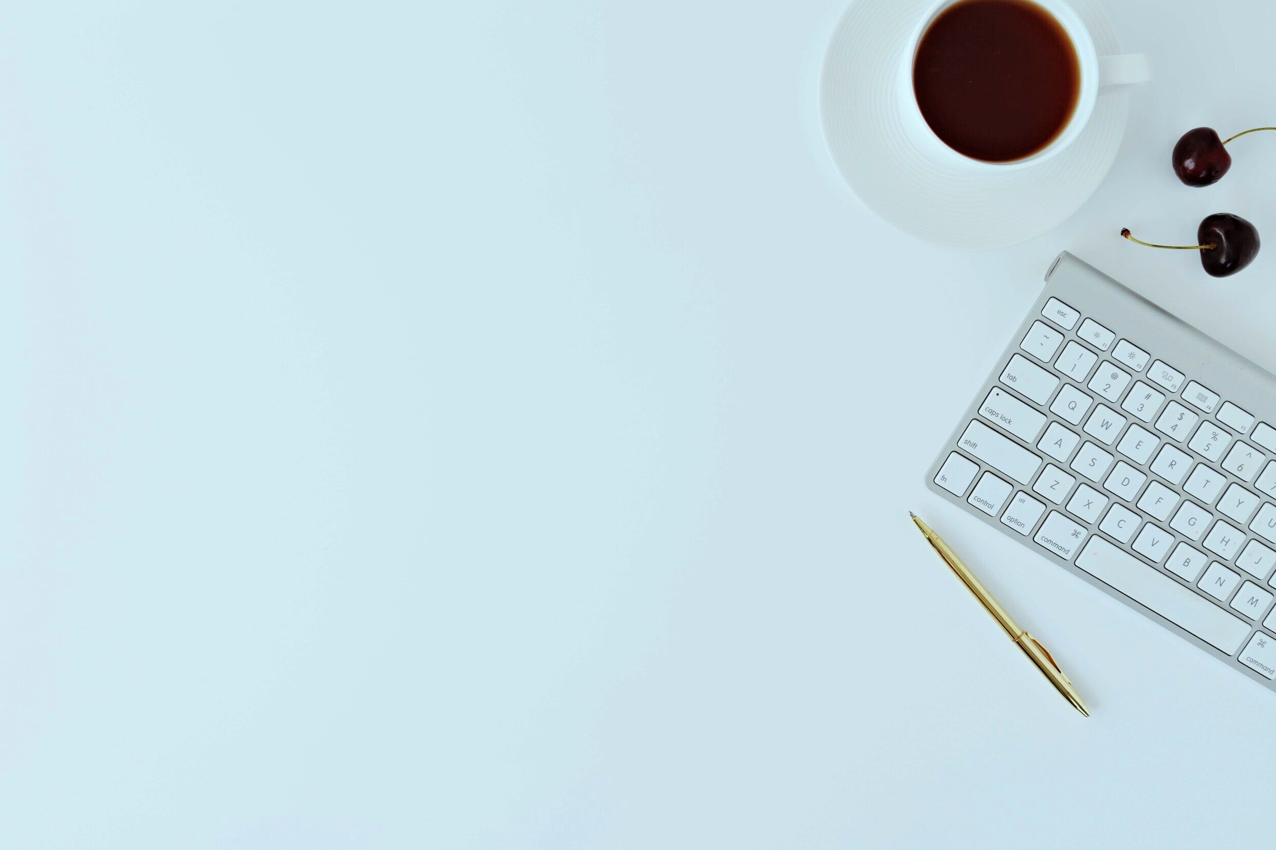 A keyboard, a gold pen, two cherries, and a cup of coffee