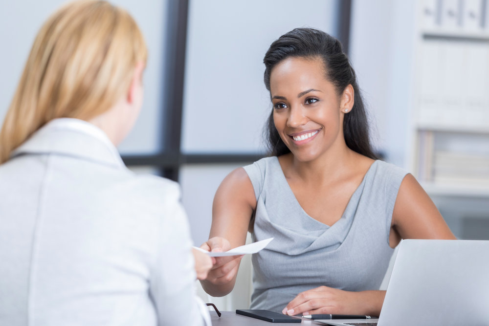 Woman giving an interview and smiling at another woman at the office while sitting at a desk.