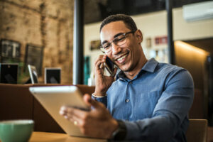 man on phone sitting with laptop smiling and in an office