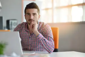 Thoughtful man sitting at a desk with a laptop, appearing to be in deep consideration—symbolizing a salesperson evaluating their next career move.